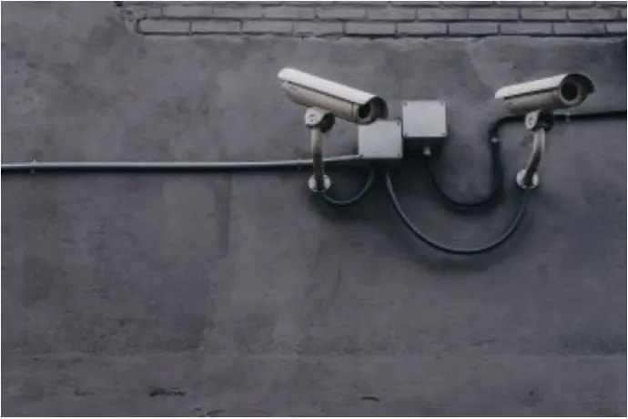 A close-up of a white security camera mounted on an external grey wall.