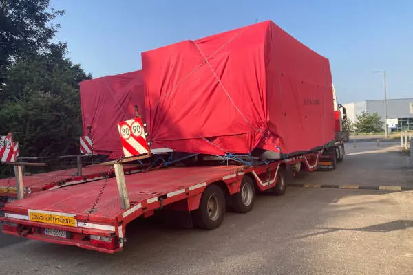 A red trailer carrying a massive piece of machinery completely wrapped in red protective film.
