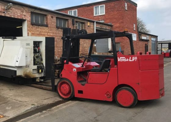 A red forklift truck parked on a paved outdoor area in front of an industrial unit.