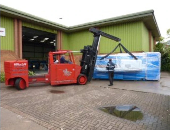 A red forklift and workers outside a large green industrial unit with a wide roller door.