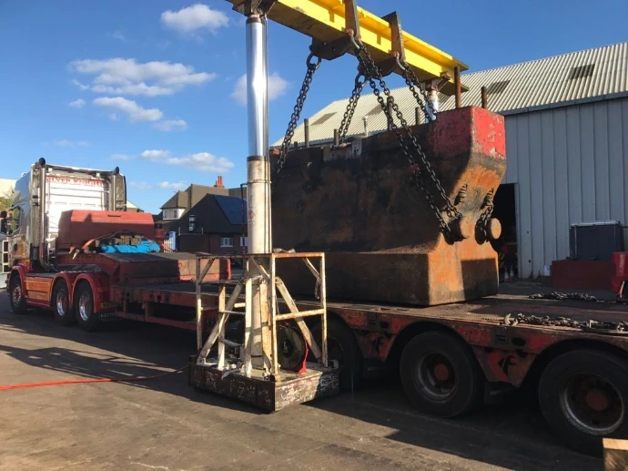 A heavy industrial unit secured with chains onto a red flatbed lorry for transport.