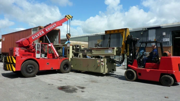 A red mobile crane lifting a heavy industrial component in an outdoor shipyard or yard.
