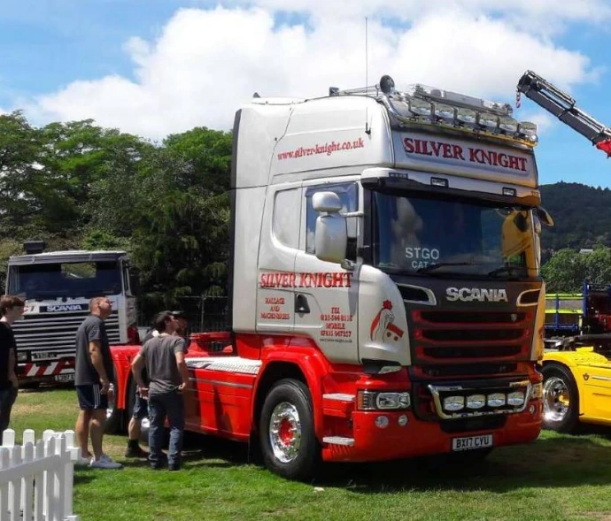 A red and white Scania lorry cab parked at an outdoor event with people nearby.