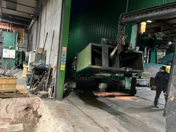 A large green industrial machine being maneuvered into a specialized factory enclosure.