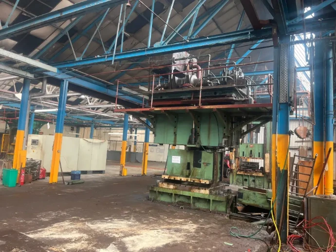 A large green industrial press machine positioned under a blue steel-frame structure.