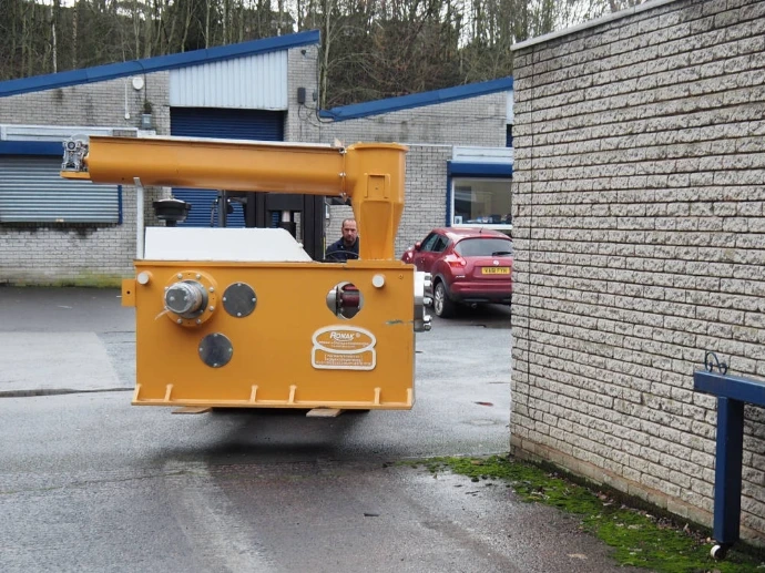 A small, yellow industrial tow tractor or utility vehicle parked on an outdoor asphalt path.